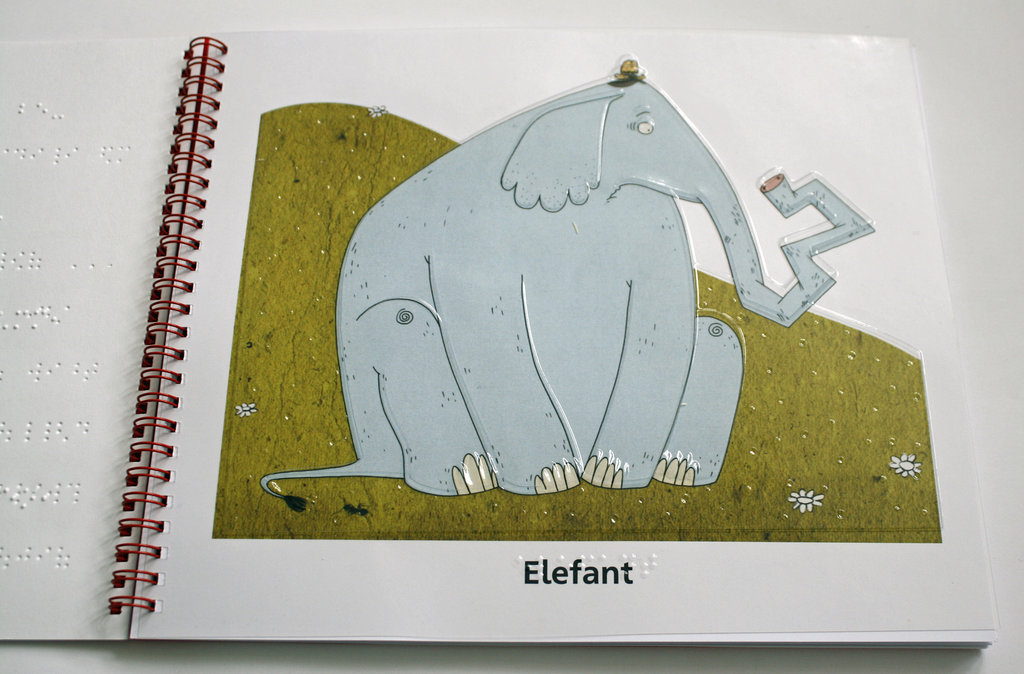 Aufgeschlagenes Buch mit Ringbindung, rechts ein Elefant, links Text in Brailleschrift und Großdruck