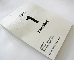 Vergrößerungsansicht: lose gelochte Kalenderblätter (in Braille- und Großschrift) auf Stapel