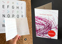 Vergrößerungsansicht: Links: Eine Hand hält eine Klappkarte mit aufgedrucktem Braillealphabet, rechts: Vorderseite Klappkarte mit Text 