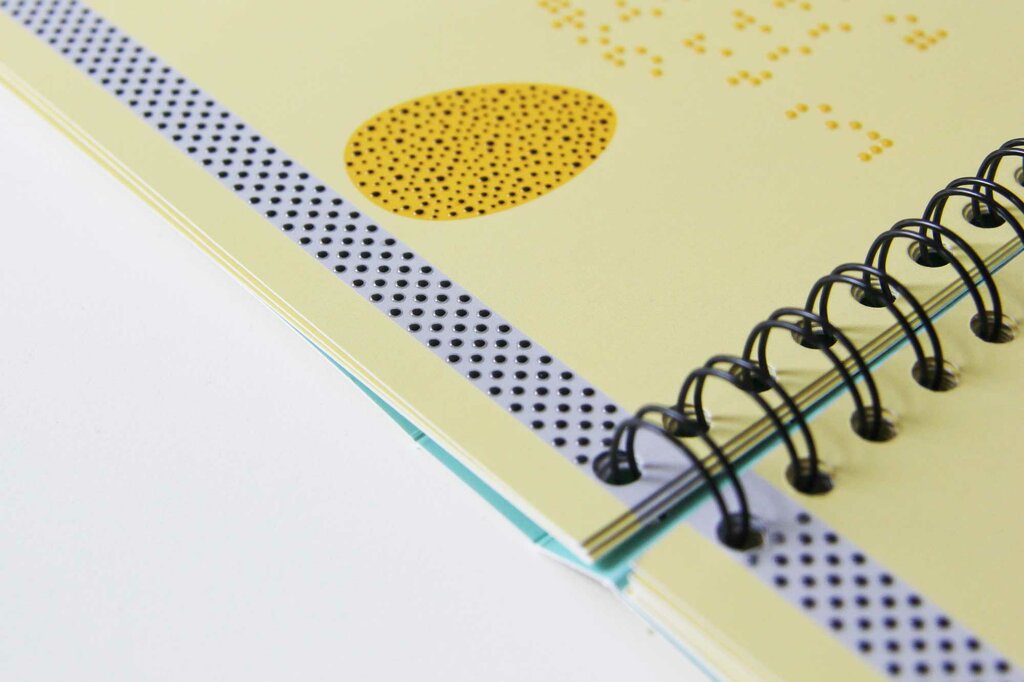 Aufgeklapptes Buch in Ringbindung im Detail mit tastbarem Ei und einer gepunkteten Linie
