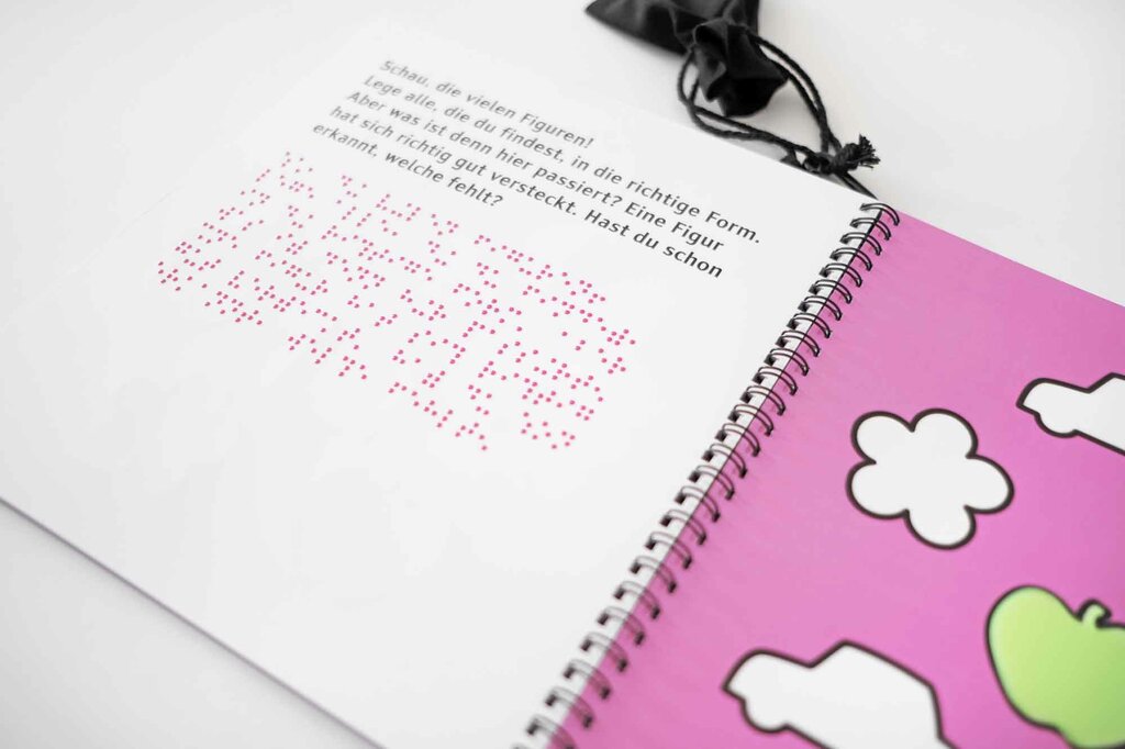Aufgeklapptes Ringbuch mit Braille-Lack, Großdruck und Lack-Konturen