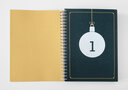 Vergrößerungsansicht: Aufgeschlagenes Ringbuch mit weißer nummerierter Weihnachtsbaumkugel auf petrolfarbenem Untergrund