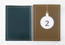 Vergrößerungsansicht: Aufgeschlagenes Ringbuch mit weißer nummerierter Weihnachtsbaumkugel auf braunem Untergrund