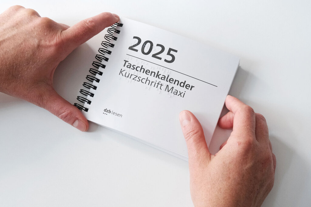 Zwei Hände halten den Taschenkalender Maxi 2025 in Brailleschrift