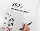 Vergrößerungsansicht: Jemand blättert mit der rechten Hand im Großdruck-Wandkalender 2025