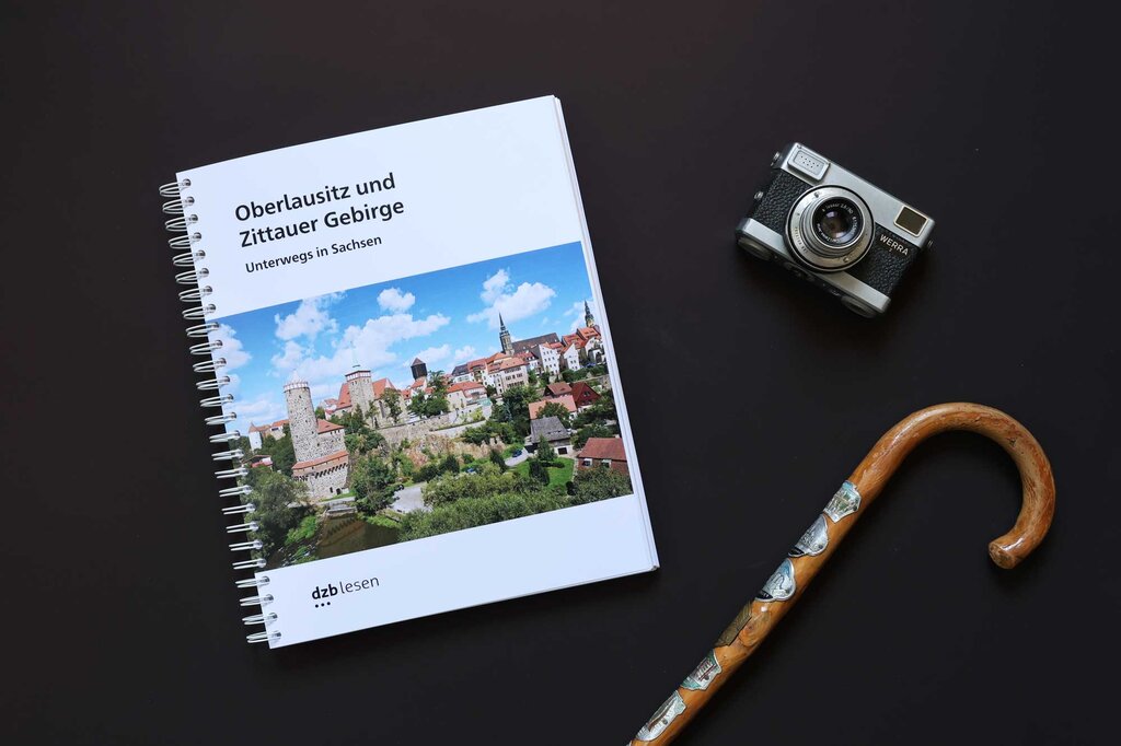 Ringbuch Reiseführer Oberlausitz und Zittauer Gebirge – unterwegs in Sachsen, ein Vintage-Fotoapparat und ein Wanderstock aus Holz auf schwarzem Untergrund.