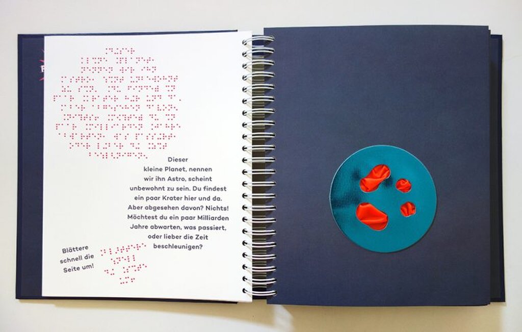 Aufgeschlagenes Ringbuch, links Text in Brailleschrift un Großdruck, rechts taktile Abbildung eines Planeten