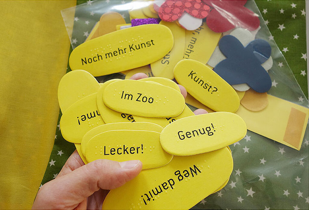 Eine Hand hält verschiedene Sticker mit Brailleschrift und Großdruck