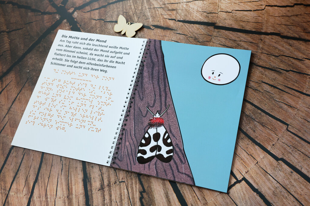 Aufgeschlagenes Ringbuch, links Text in Großdruck und Brailleschrift, rechts Illustration einer schwarz-weißen Motte auf einem Baumstamm, rechts darüber leuchtet der weiße Mond.
