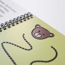 Vergrößerungsansicht: Detailausschnitt einer Seite aus dem Rätselheft »Besuch im Zoo«, abgebildet ist ein taktil gedruckter Bärenkopf, darunter angedeutet eine gepunktete Schlängellinie, ebenfalls tastbar mit Braillelack gedruckt.