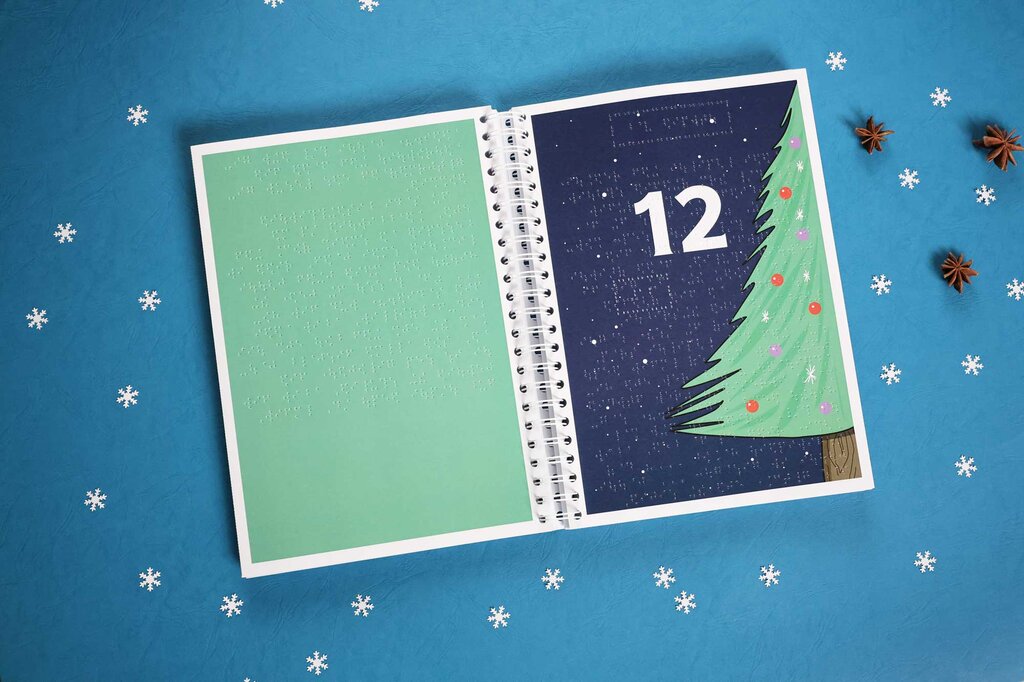 Aufgeklappter Adventskalender mit Brailleschrift und Illustration eines Weihnachtsbaums mit Baumschmuck.