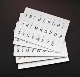Ein Stapel mit Postkarten mit tastbarem Brailleschrift-Alphabet in farbigem Lackdruck.