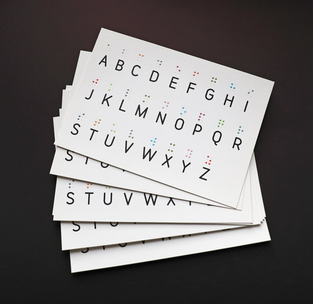 Ein Stapel mit Postkarten mit tastbarem Brailleschrift-Alphabet in farbigem Lackdruck.