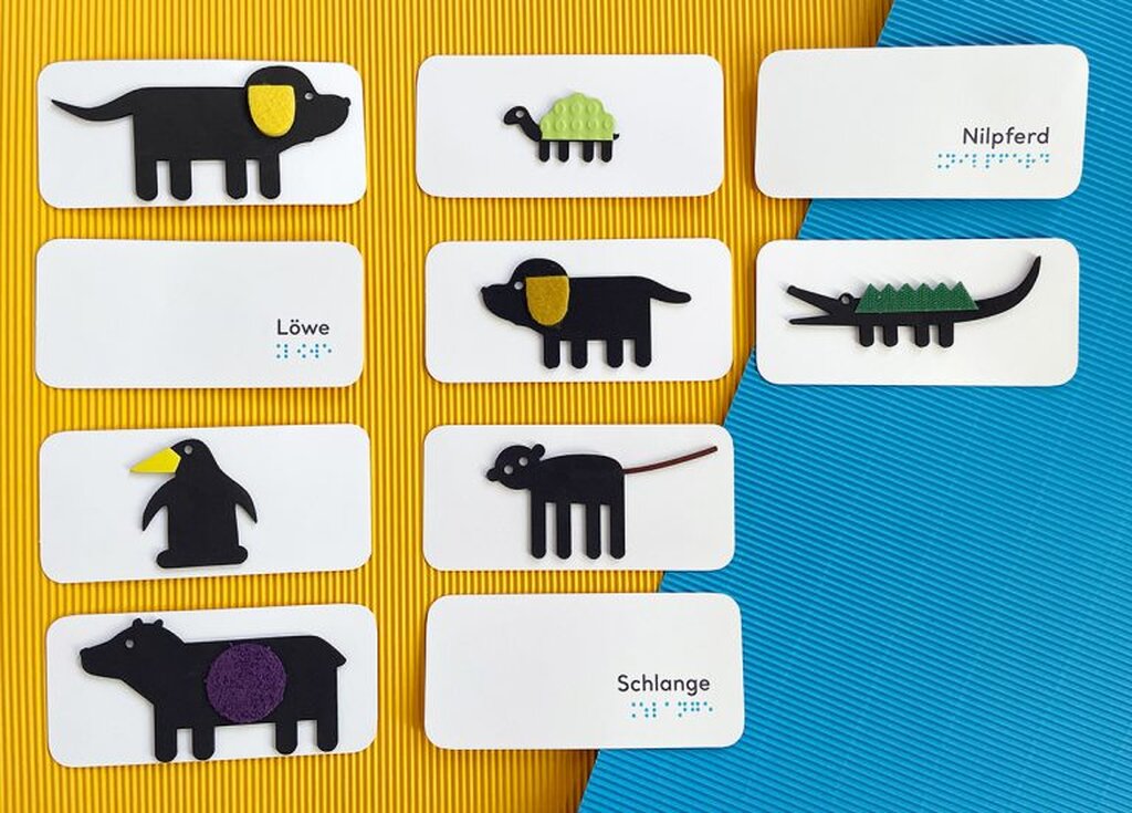 Zehn taktil gestaltete Spielkarten liegen ausgebreitet auf farbiger Wellpappe und zeigen die verschiedenen Tiere, die im Buch vorkommen: Hund Spot, Schildkröte, Krokodil, Pinguin, Affe, Bär und Hundemama Sally.