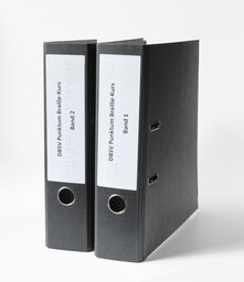 Zwei stehende Ringordner im A4-Format mit Beschriftung in Brailleschrift und Großdruck.